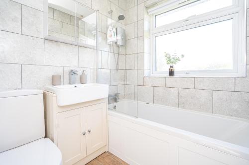 a white bathroom with a sink and a tub and a window at Spacious 5 Bedroom House - Sleeps 7 - 3-Car Driveway - Work - Leisure in Wolverhampton