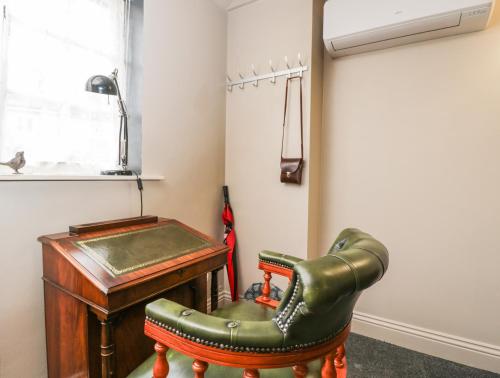 Cette chambre comprend un bureau et un fauteuil en cuir vert. dans l'établissement Paddock Cottage, à Malmesbury