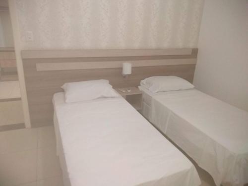 2 Betten in einem kleinen Zimmer mit weißer Bettwäsche in der Unterkunft HOTEL APARECIDA in Rodeio Bonito