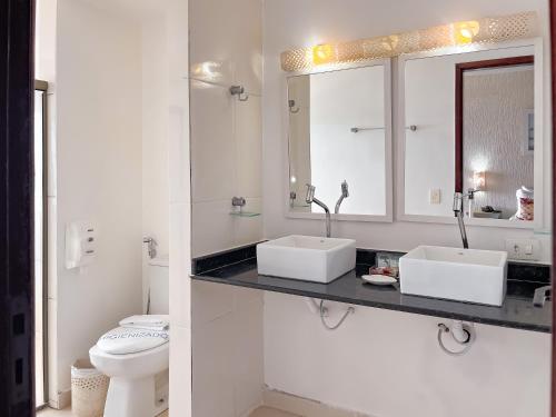 a white bathroom with two sinks and a toilet at Pousada do Albatroz in Cabo Frio