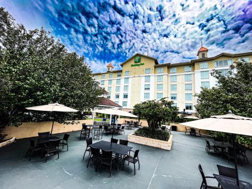 un patio del hotel con mesas, sillas y sombrillas en Holiday Inn - St Augustine - World Golf, an IHG Hotel, en St. Augustine
