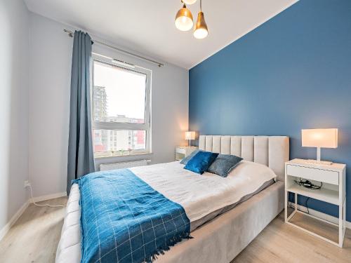 a bedroom with a bed with blue walls and a window at Hello Apartments Letnica with private parking in Gdańsk