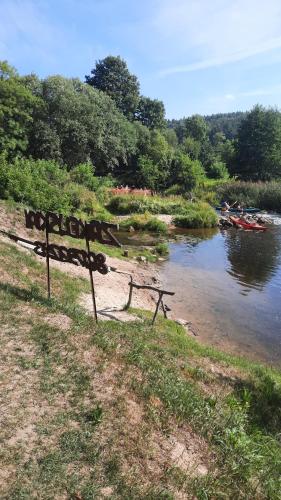 a sign sitting on the side of a river at Zakeliškių vandens malūno stovyklavietė in Zakeliškiai