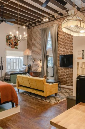 a living room with a yellow couch and a brick wall at Historic Garden Studio, Steps from Pulaski Square in Savannah