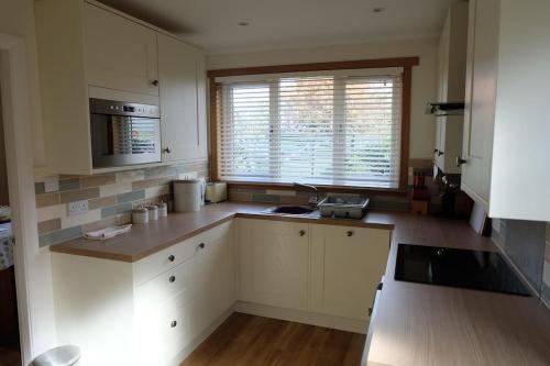 uma cozinha com armários brancos, um lavatório e uma janela em Isla Cottage em Blairgowrie