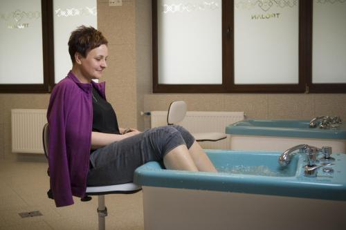 a woman sitting in a chair next to a sink at Hotel Trojan in Lądek-Zdrój