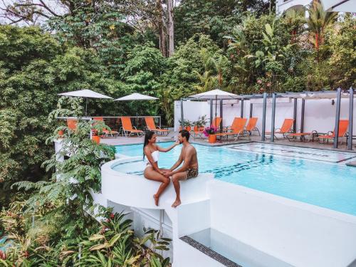 a couple sitting on the edge of a pool at a hotel at Shana by the Beach Manuel Antonio in Manuel Antonio