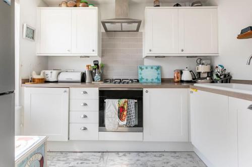 a white kitchen with white cabinets and an oven at Hideaway Cottage - seaview room with shared bathroom in Sandgate