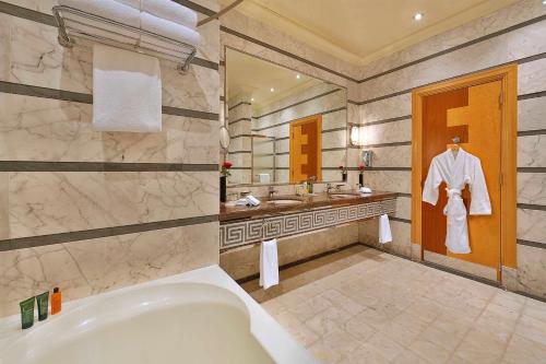 a bathroom with a tub and two sinks and a robe on a door at Jeddah Hilton in Jeddah