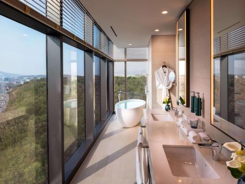 DoubleTree By Hilton Seoul Pangyo في سيونغنام: حمام مع حوض ومغسلة ونوافذ كبيرة