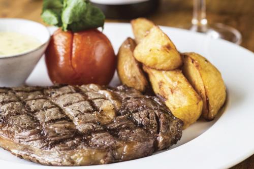 a steak with potatoes and a tomato on a plate at The Old Stocks Inn in Stow on the Wold