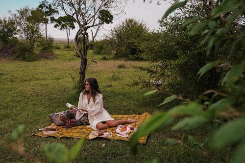 a woman sitting on a blanket on the grass at Enkusero Mara in Aitong