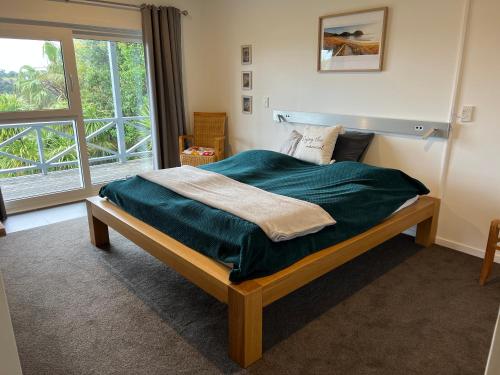 a bedroom with a bed with a green blanket and a window at Tutukaka Sunrise in Tutukaka