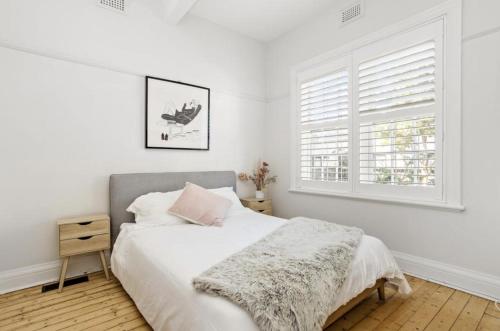 NEWLY RENOVATED LARGE 3.5 BDRM HOUSE! BEST OF MELB في ملبورن: غرفة نوم بيضاء بها سرير ونافذة