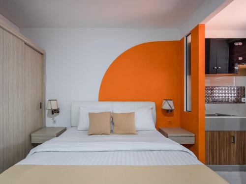1 dormitorio con 1 cama blanca grande y pared de color naranja en Cove Taman, en Yakarta