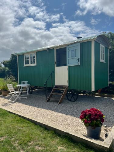 a green tiny house with a table and chairs at Toms Hut and Robins Rest Shepherd Huts near Wadebridge in Wadebridge