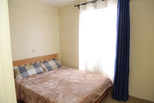 a bedroom with a bed with blue curtains and a window at Rooftop Haven Allsoaps in Nairobi