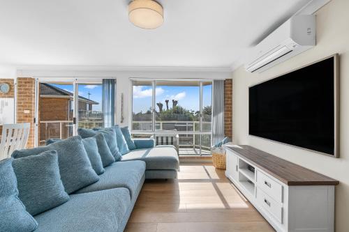 ein Wohnzimmer mit einem blauen Sofa und einem Flachbild-TV in der Unterkunft Bella Vista: Ocean views a short stroll to beach. in Mollymook