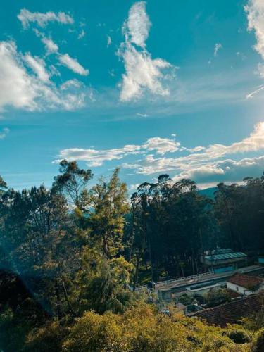 a group of trees and a blue sky with clouds at Nama-Stay - An escape villa in Ooty