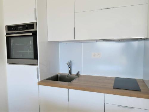 une cuisine blanche avec un évier et un micro-ondes dans l'établissement Bel appartement rénové face au port avec loggia et garage privé à Perros-Guirec - FR-1-368-283, à Perros-Guirec