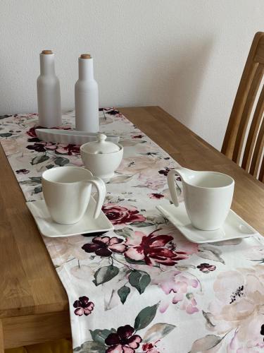 una mesa con dos tazas y platos en un mantel floral en Albblick en Albstadt