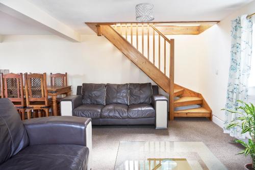 a living room with a leather couch and a staircase at The Barn (Chilsworthy), 6 Sleeper House, 19 Min Drive into Bude, Cornwall in Holsworthy