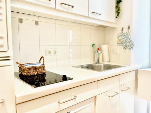 eine weiße Küche mit einem Waschbecken und einem Korb auf der Theke in der Unterkunft Wohlfühl Strand Wohnung 'Mein Ankerplatz' in Lübeck