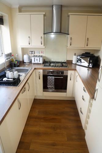 a kitchen with a sink and a stove top oven at Luxe Cosy&Spacious 2 Bed House - Super Fast Wi-Fi & Private Parking Near GLO Airport & Cheltenham Racecourse in Churchdown
