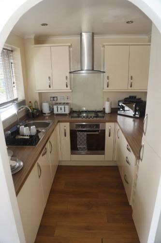a kitchen with white cabinets and a stove top oven at Luxe Cosy&Spacious 2 Bed House - Super Fast Wi-Fi & Private Parking Near GLO Airport & Cheltenham Racecourse in Churchdown