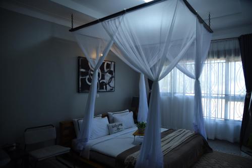 a bedroom with a canopy bed with curtains and a window at Gamaleo Apartment Namulanda in Namulanda