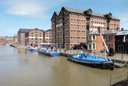 three boats are docked in a river with buildings at Luxe Cosy&Spacious 2 Bed House - Super Fast Wi-Fi & Private Parking Near GLO Airport & Cheltenham Racecourse in Churchdown