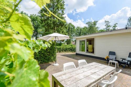 a patio with a wooden table and chairs and an umbrella at Chalet Oakley I Ontspan in de natuur in Putten