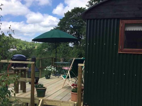 a wooden deck with a green umbrella and a table at Shepherd's Hut. Shower & WC. Deck. Amazing view in Longhope