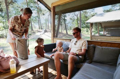 un homme et une femme et un bébé assis sur une terrasse couverte dans l'établissement Familie vakantiepark Krieghuusbelten, à Raalte