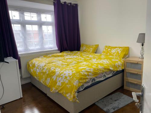 a bedroom with a bed with a yellow comforter and a window at London Heathrow Homes in New Bedfont