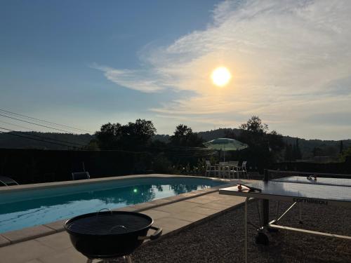 a grill next to a swimming pool with the sun in the sky at Villa Chante Grive in Taradeau