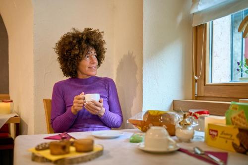 a woman sitting at a table holding a cup at DolceVita Ambiez B&B in San Lorenzo in Banale