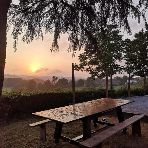 una mesa de picnic bajo un árbol con la puesta de sol en el fondo en Les trois jolies 