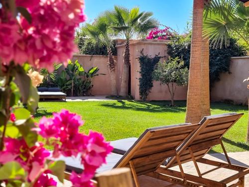 a wooden chair sitting in a yard with pink flowers at Villa avec gouvernante et 2 piscines dont une chauffée dans domaine securise in Marrakesh