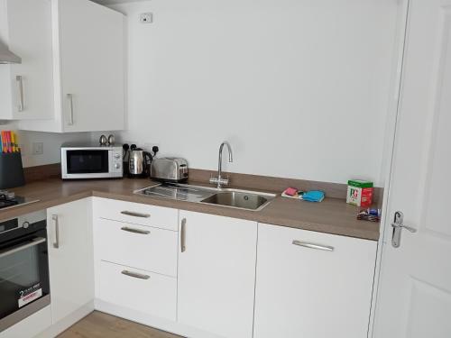 eine Küche mit weißen Schränken, einer Spüle und einer Mikrowelle in der Unterkunft Quality City - Central Birmingham in Birmingham