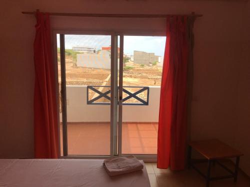 a bedroom with a bed and a window with red curtains at Maio Relax in Vila do Maio