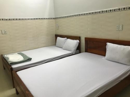 2 bedden in een kleine kamer met witte lakens bij Nhà nghỉ Bình An - Binh An Motel in Quang Tri