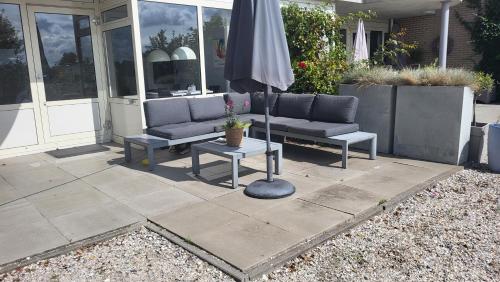 a patio with two couches and an umbrella at Duinzicht, ruim appartement met terras op de begane grond nabij strand in Buren
