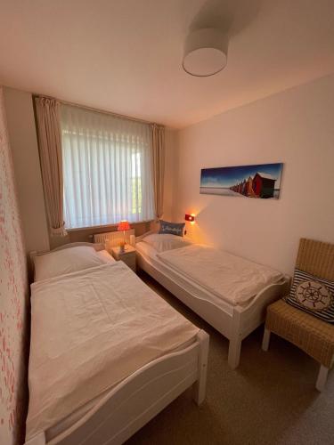 a bedroom with two beds and a window and a chair at Haus-Seeschwalbe-Wohnung-3 in Nieblum