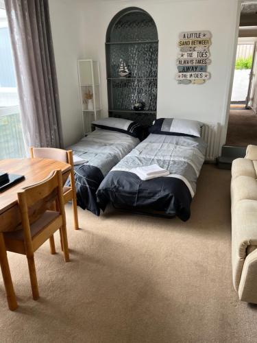 two beds in a room with a table and a couch at Primrose Steps in Goodrington