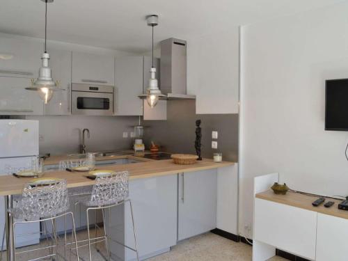 une cuisine avec des placards blancs et un comptoir avec des tabourets de bar dans l'établissement Appartement rénové, climatisé à 200m de la plage avec balcon et parking privé - FR-1-229D-12, à Fleury