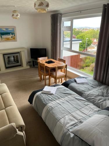 a bedroom with two beds and a table and a window at Primrose Steps in Goodrington