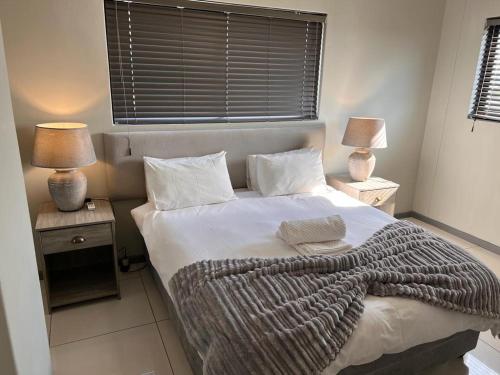 a bedroom with a bed with a blanket and two lamps at Le grand Hideout in Windhoek