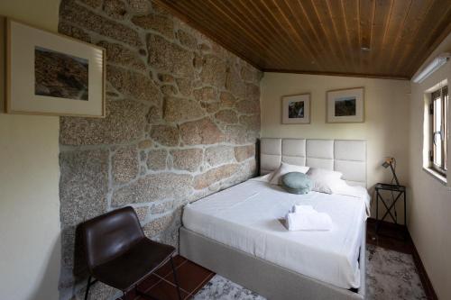 a bedroom with a bed with a chair and a stone wall at Casa da Cascata in Pincães