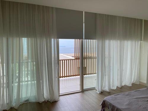a bedroom with white curtains and a large window at Villa 60 b - Palasë in Palasë